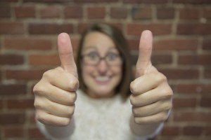 Smiling woman with glasses giving two thumbs up in front of a brick wall, expressing positivity about the home appraisal process.