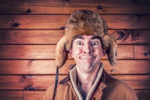 Man making a funny face while wearing a fur hat, against a wooden background, representing a lighthearted approach to first-time home buyer loans.