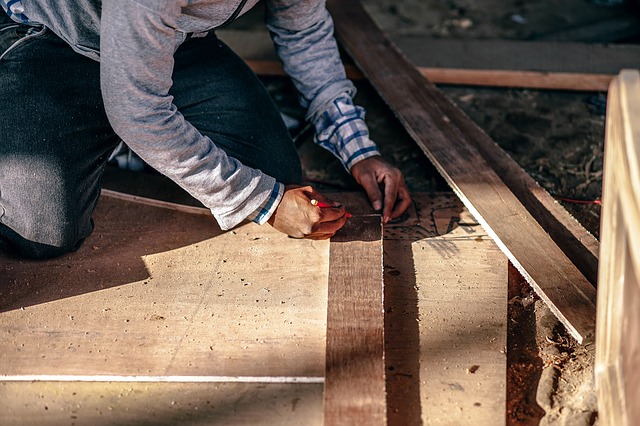 Person measuring and marking wooden boards for renovation, illustrating home improvement and construction related to FHA 203K loans.